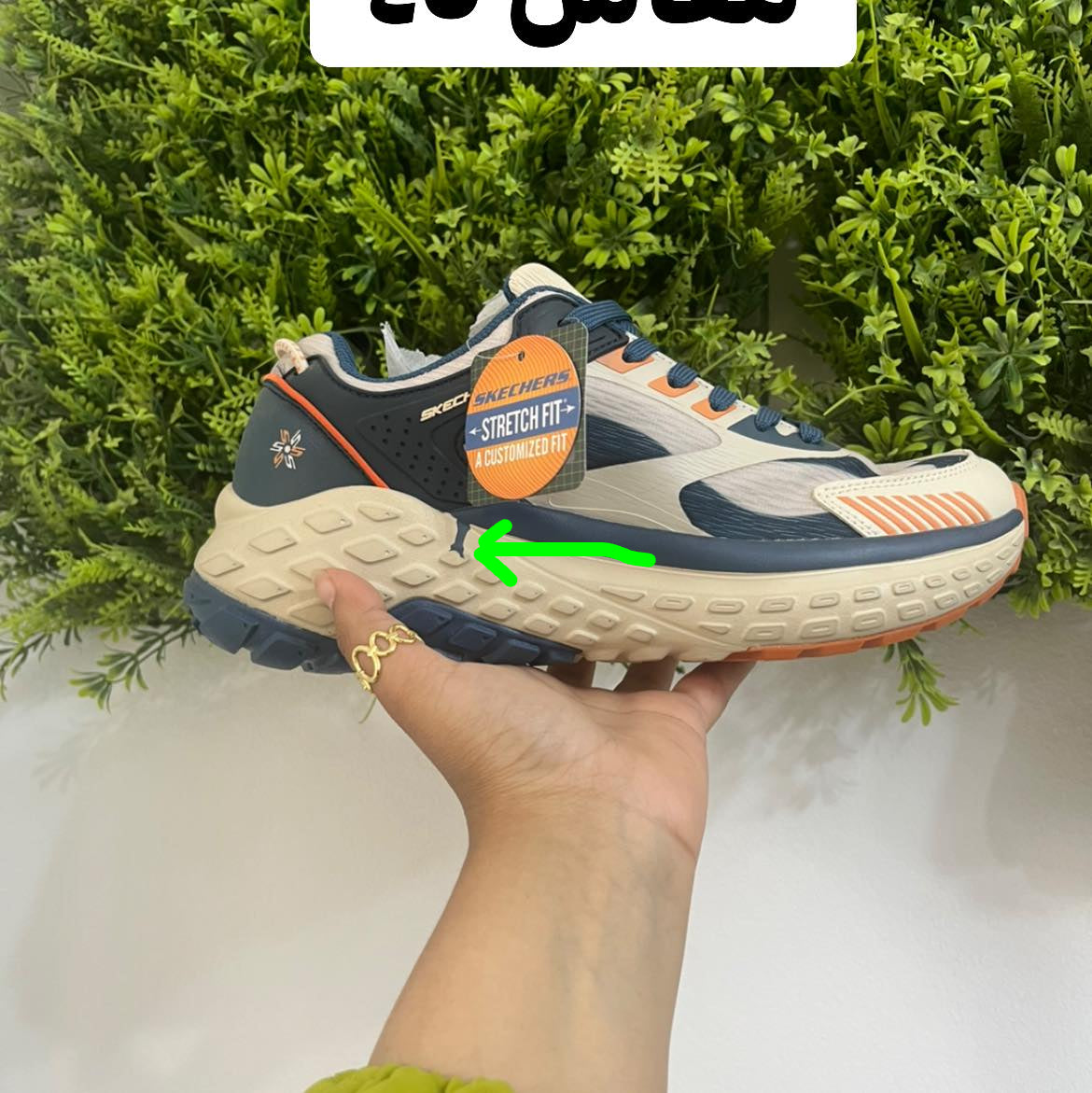 Person holding a running shoe with a 'Skechers' tag against a green leafy background