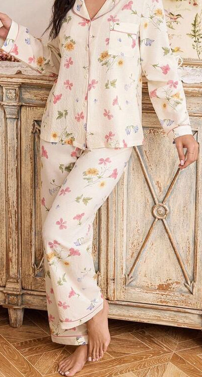Woman in floral pajama set reading a book in a room with wooden furniture and decorative elements.